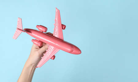 Hand holding pink air plane on blue background. Minimalism travel concept