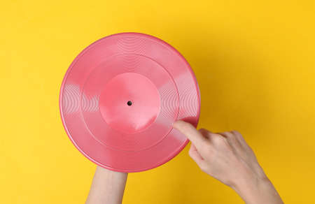 Female hands holding pink vinyl record on yellow background. DJ, music conceptの写真素材