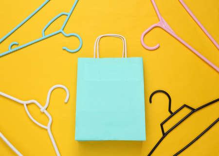 Hangers and paper shopping package on yellow background. top view. minimalismの写真素材