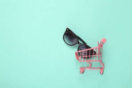 Pink mini shopping cart with sunglasses on blue backgroundの写真素材