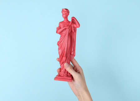 Hand holding pink antique statue on blue backgroundの写真素材
