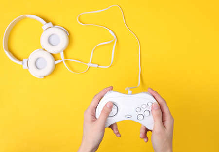 Female hands hold retro gempads on yellow background with headphones. gaming concept