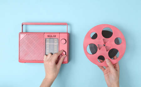Female hands tunes pink fm radio receiver and holding audio reel on blue background. Music minimal conceptの写真素材