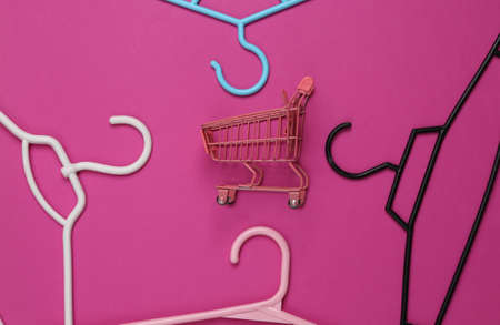 Plastic hangers with mini shopping trolley on pink background. fashion layout. flat lay. top view