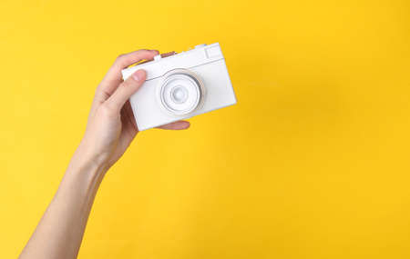Hands holding white camera on yellow background. minimalism