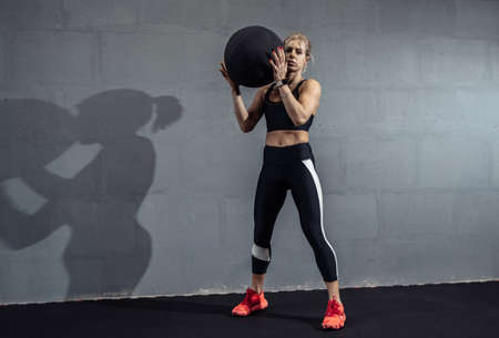 Sportswoman doing stretching exercise with medicine ball. Muscular woman exercising fitness ball at...