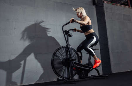 Woman doing intense cardio training on exercise bike. Fitness female using air bike for cardio...