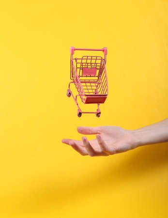 Hand and Levitating pink shopping trolley on yellow background. Minimalistic still life. concept art. video gamesの写真素材