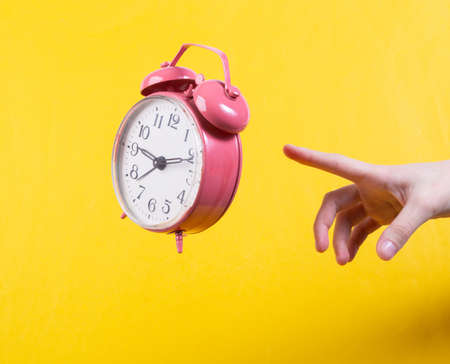 Hand and Levitating pink alarm clock on yellow background. Minimalistic still life. concept artの写真素材