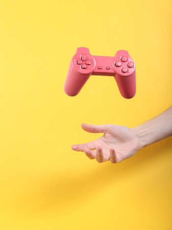 Hand and Levitating pink gamepad on yellow background. Minimalistic still life. concept art. video gameの写真素材