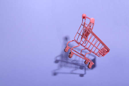 Levitating pink shopping trolley on purple background with shadow. 3D photo. Minimalistic still life. creative layout. concept artの写真素材