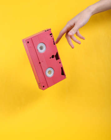 Hand and Levitating pink video cassette on yellow background. Minimalistic still life. concept art. video gameの写真素材