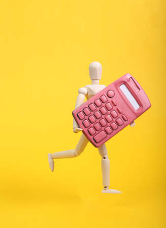 Wooden puppet holding pink calculator on yellow backgroundの写真素材
