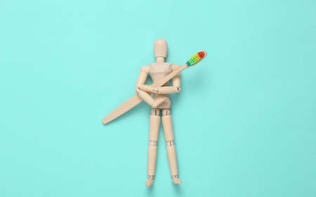 Wooden puppet holding rainbow Eco-friendly bamboo toothbrush on blue background.