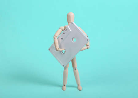 Wooden puppet holding white audio cassette on blue backgroundの写真素材