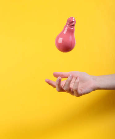 Hand and Levitating pink light bulb on yellow background. Minimalistic still life. concept art. video gameの写真素材