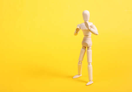 Wooden puppet in combat stance on yellow background