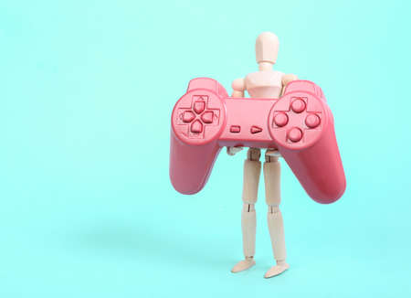 Wooden puppet holding pink gamepad on blue backgroundの写真素材