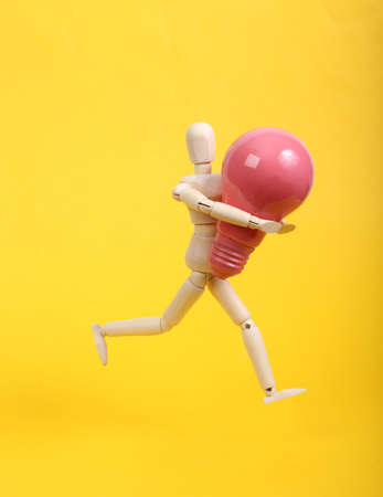 Wooden puppet holding pink light bulb on yellow backgroundの写真素材
