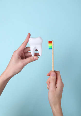 Hands holding Eco-friendly bamboo toothbrush and tooth on blue background. Dental care concept. top...