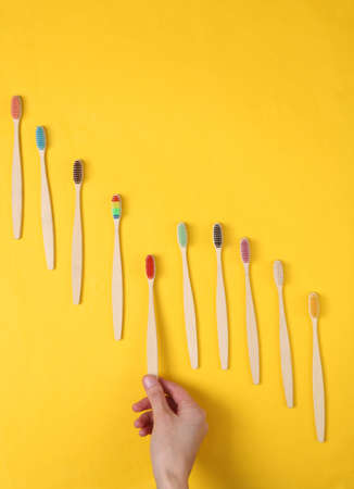 Hand selects Eco-friendly bamboo toothbrush among the set on yellow background