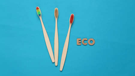 Eco-friendly bamboo toothbrushes and word eco on blue background. top view.