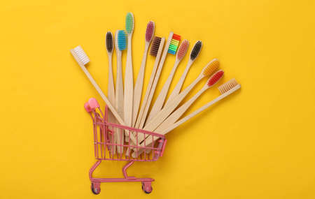 Mini shopping trolley with Eco-friendly bamboo toothbrushes on yellow background.
