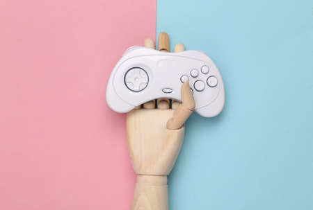 Wooden hand holding White painted gamepad on blue pink background. minimalism. concept art