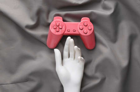 Hand and pink gamepad on gray silk background.