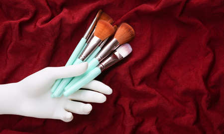 White hand holding Makeup brushes on red silk background. beauty still life.の写真素材