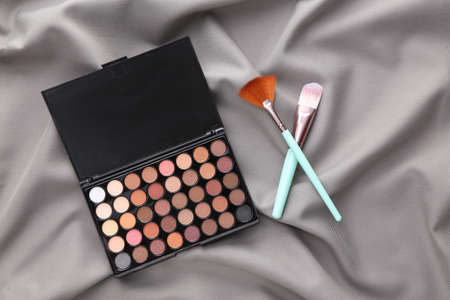Bright make up eye shadow palette and Makeup brushes on gray silk background. beauty still life.