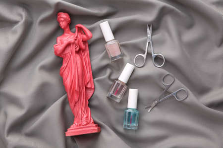 Antique pink statue, bottle of nail polish, scissors on gray silk background. beauty conceptの写真素材