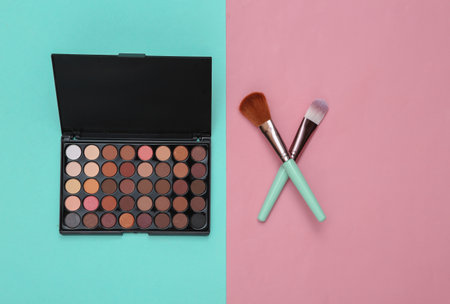 Bright make up eye shadow palette and Makeup brushes on pink blue background. beauty still life. flat layの写真素材