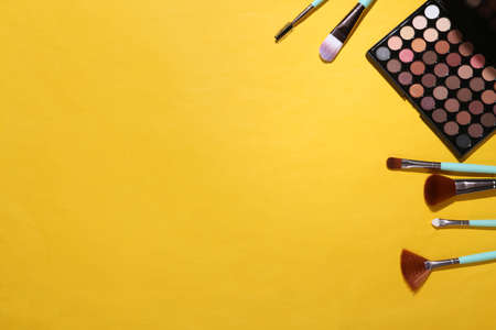 Women's accessories. Beauty products on yellow background. Make up eye shadow palette, makeup brushes. top view. copy spaceの写真素材