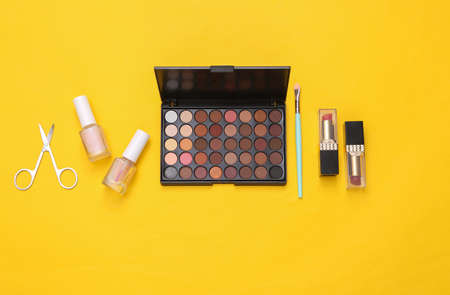 beauty products on yellow background. Make up eye shadow palette, makeup brushes, scissors and nail polish. top view. flat layの写真素材