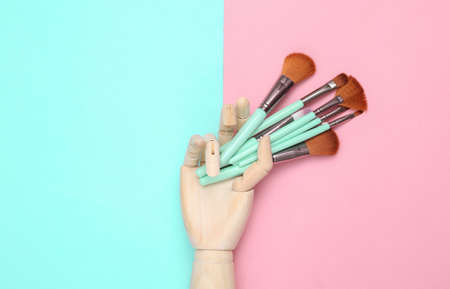 Wooden hand holding Makeup brushes on pink blue background. beauty layout. flat lay. minimalismの写真素材