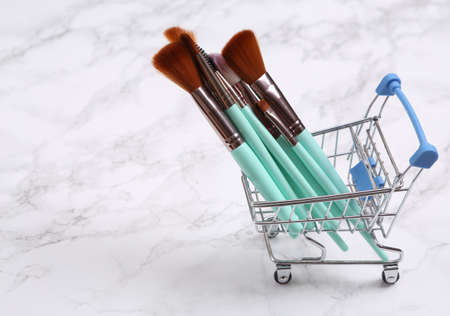 Shopping cart with makeup brushes on marble background