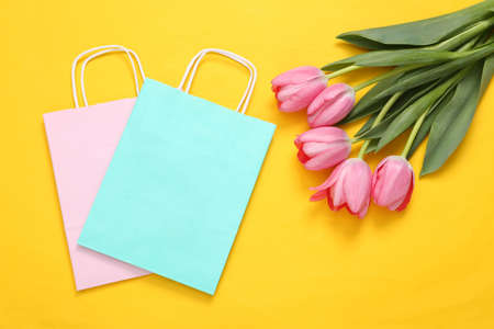 Shopping bags and pink tulips on yellow background. Romantic, shopping, holiday conceptの写真素材
