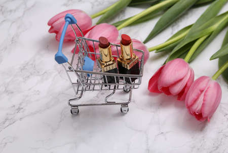 Shopping cart with lipstick and bouquet of tulips on marble surfaceの写真素材