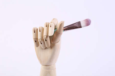 Wooden hand holds a make-up brush on a white background. beauty still lifeの写真素材
