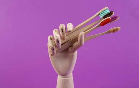 Wooden hand holding many eco bamboo toothbrushes on purple backgroundの写真素材