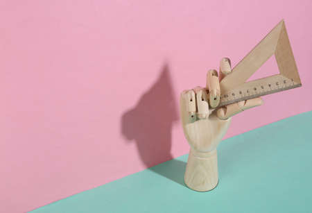 Wooden hand holding triangle ruler on blue pink pastel background. trendy shadow. concept art....