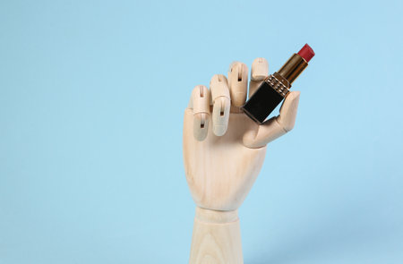 Wooden hand holding lipstick on blue background