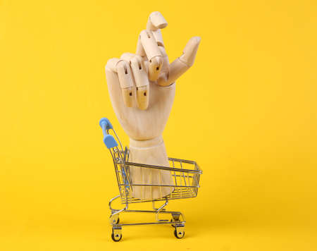 Wooden hand in shopping cart on a yellow background