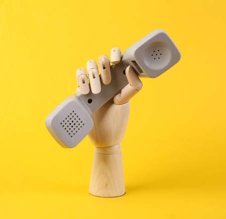 Wooden hand holding phone tube on yellow background