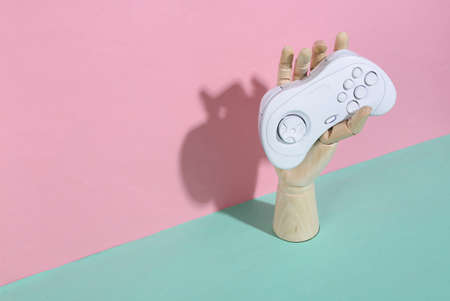 Wooden hand holding gamepad on blue pink pastel background. trendy shadow. concept art. minimalism....