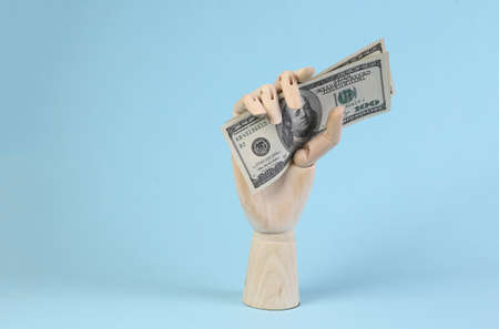 Wooden hand holding dollar bills on blue background