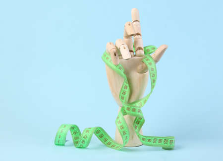 Wooden hand wrapped in measuring tape on blue background. weight loss, diet conceptの写真素材