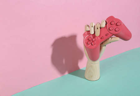 Wooden hand holding pink gamepad on blue pink pastel background. trendy shadow. concept art. minimalism. creative layoutの写真素材