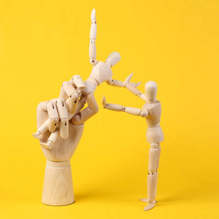 Wooden Hand holds a puppet on a yellow background. controlの写真素材